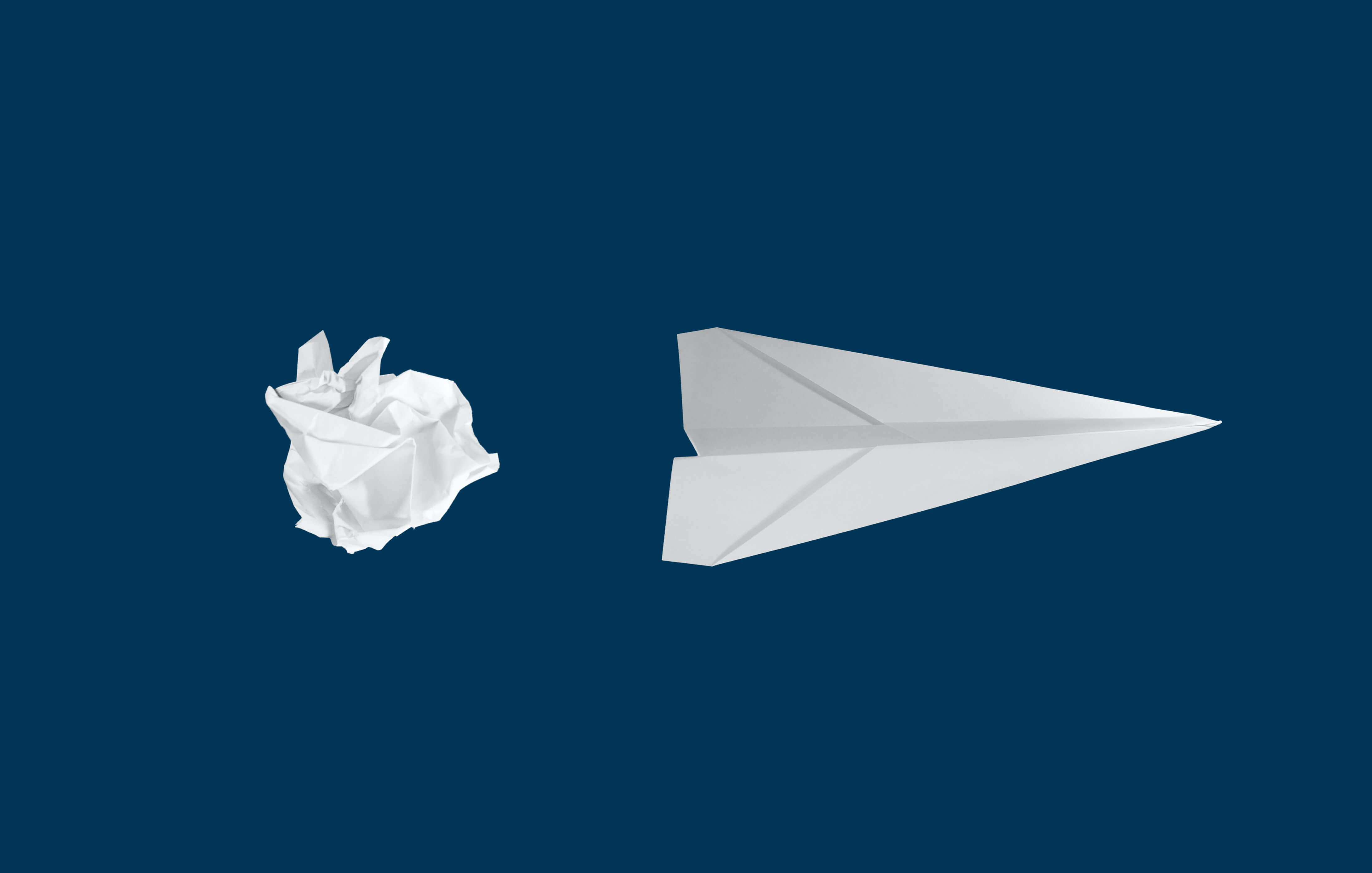 Crumpled up paper next to a paper airplane