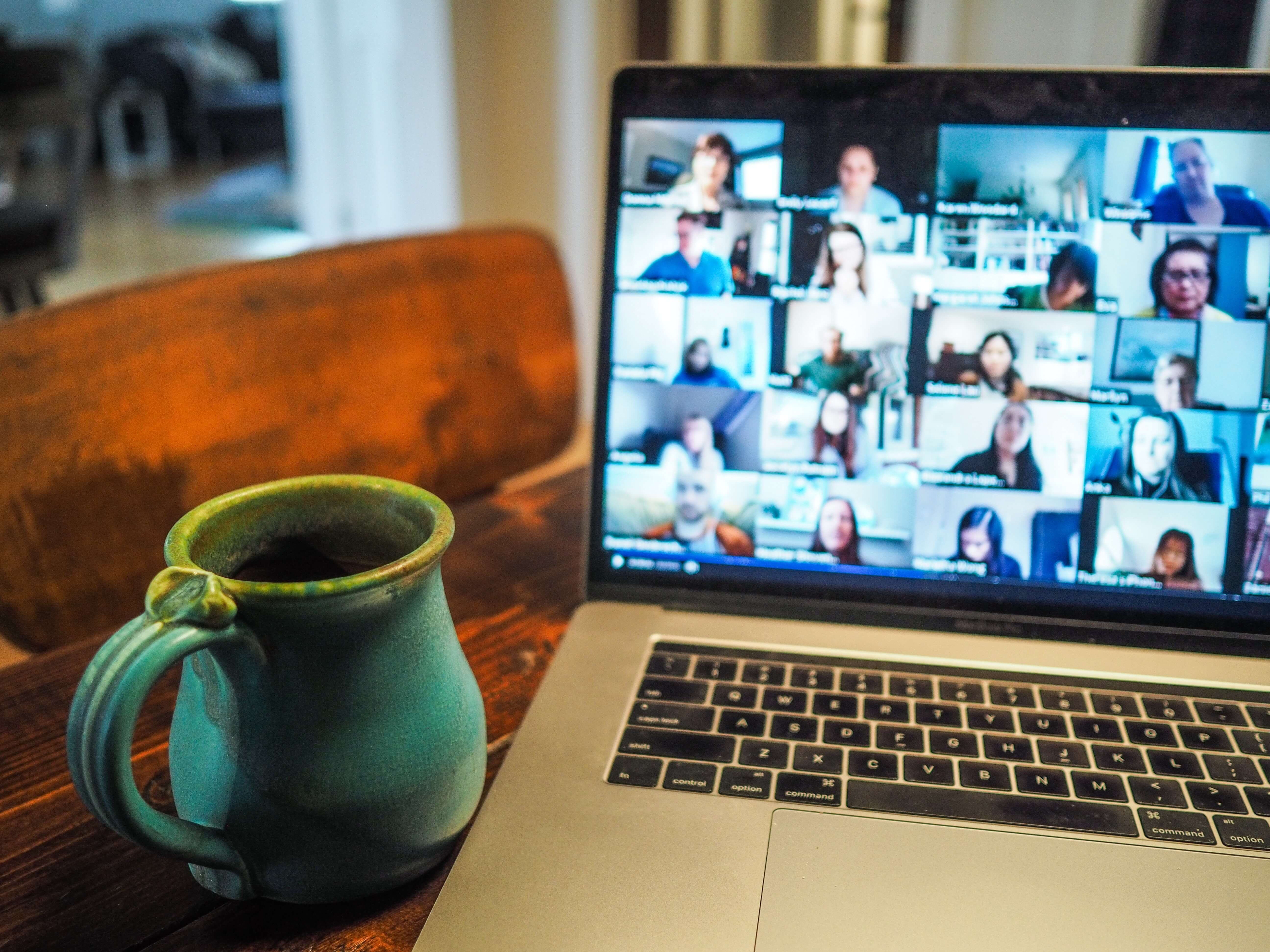 Computer showing a zoom meeting sitting on a desk next to a coffee cup.